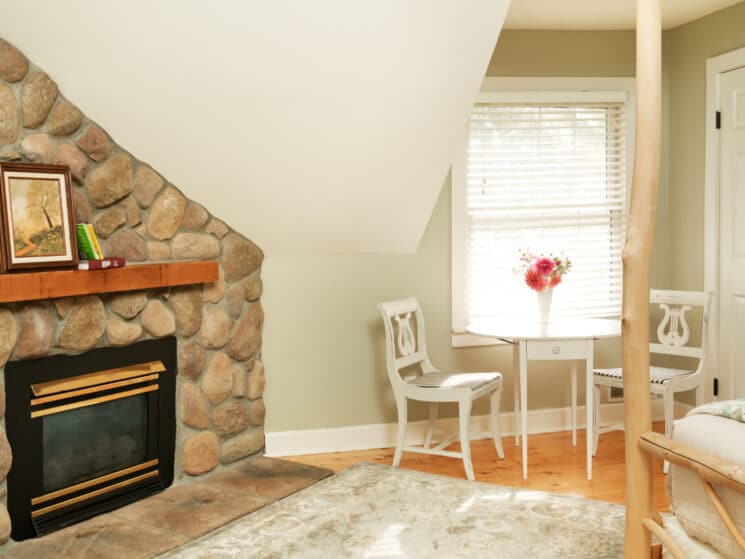 Small white table and two chairs by a window and stone fireplace