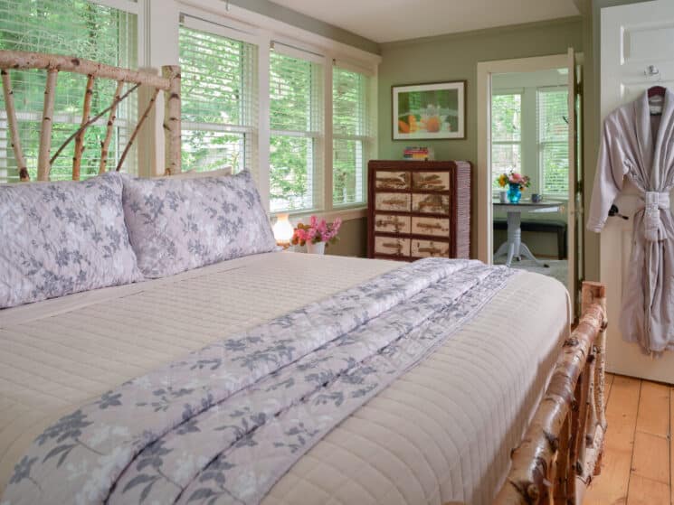 White Birch bed with row of windows, a birch chest of drawers, and an open doorway into another room with a table and colorful flowers in a blue vase.