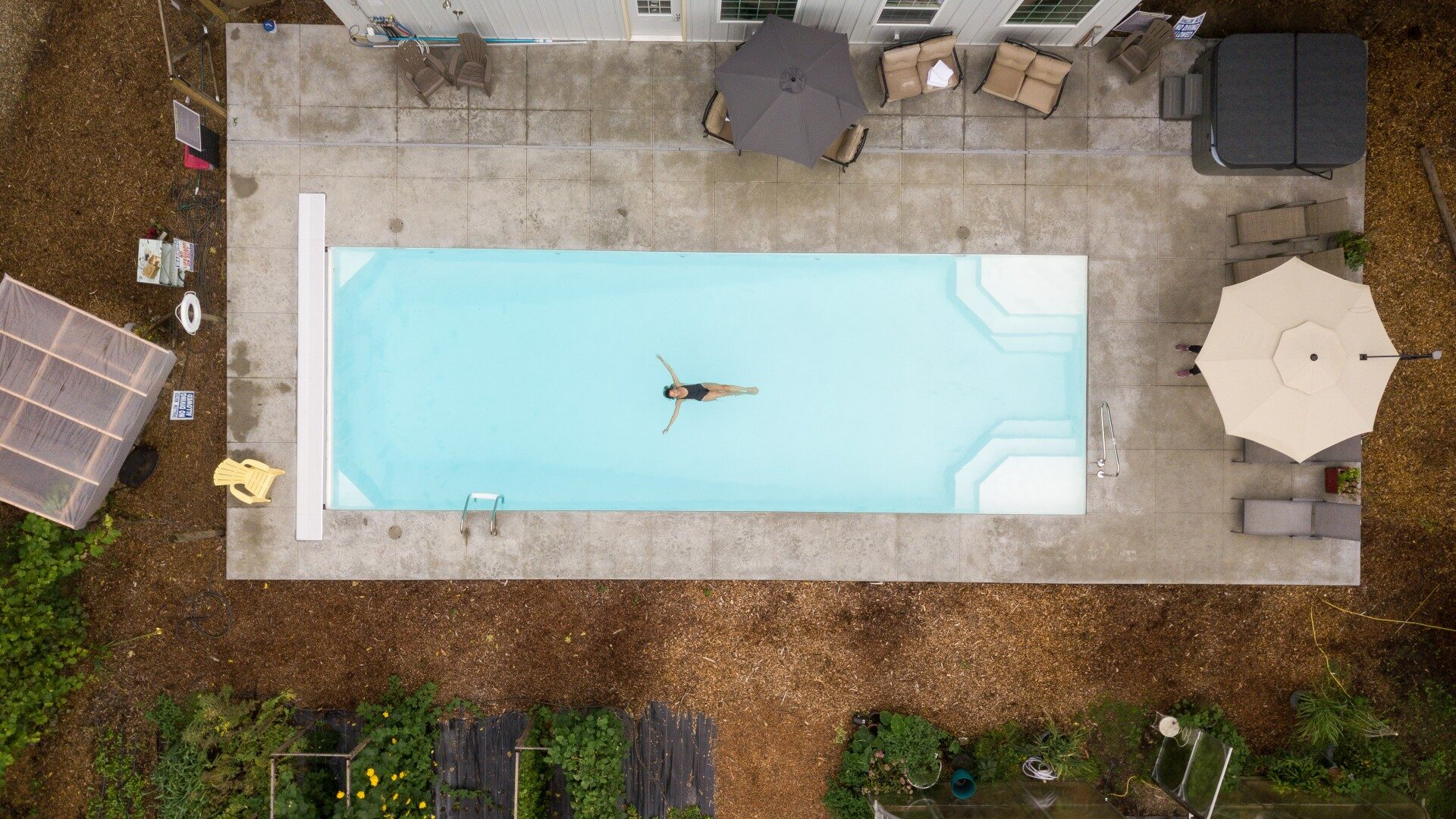 Overhead view of a large outdoor swimming pool next to a building surrounded by plants