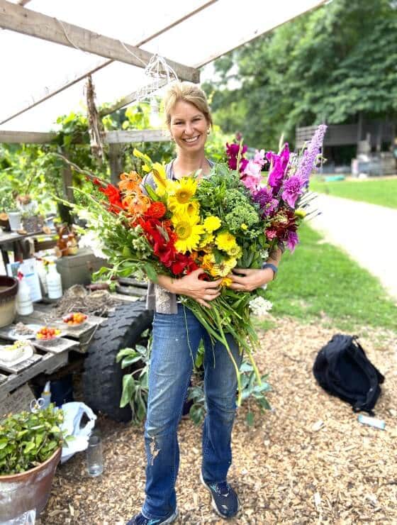 A woman in jeans outside holding a large bouquet of freshly cut flowers