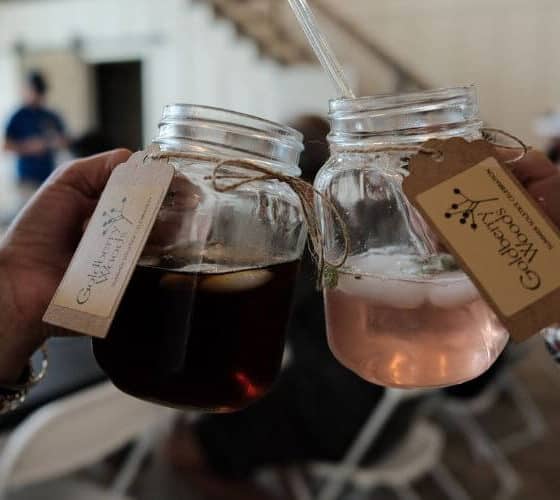 hands holding two mason jar glasses clinking together with cold drinks.