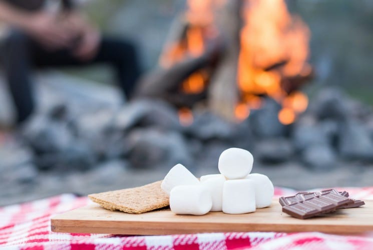 Graham crackers, marshmallows and chocolate on a wood tray atop a red and white checkered blanket