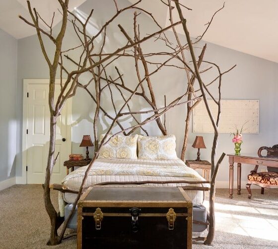 Bright and cozy bedroom with custom queen bed with rustic branch details, chest and writing desk near a large window with curtains
