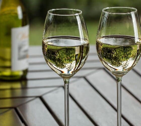 Two glasses of white wine next to a bottle on an outdoor table