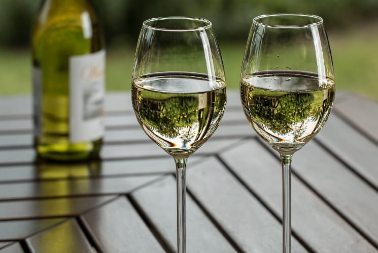 Two glasses of white wine next to a bottle on an outdoor table