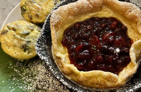 Dutch Baby Pancake in a cast iron skillet. filled with Fresh Berry compote and dusted with powdered sugar.