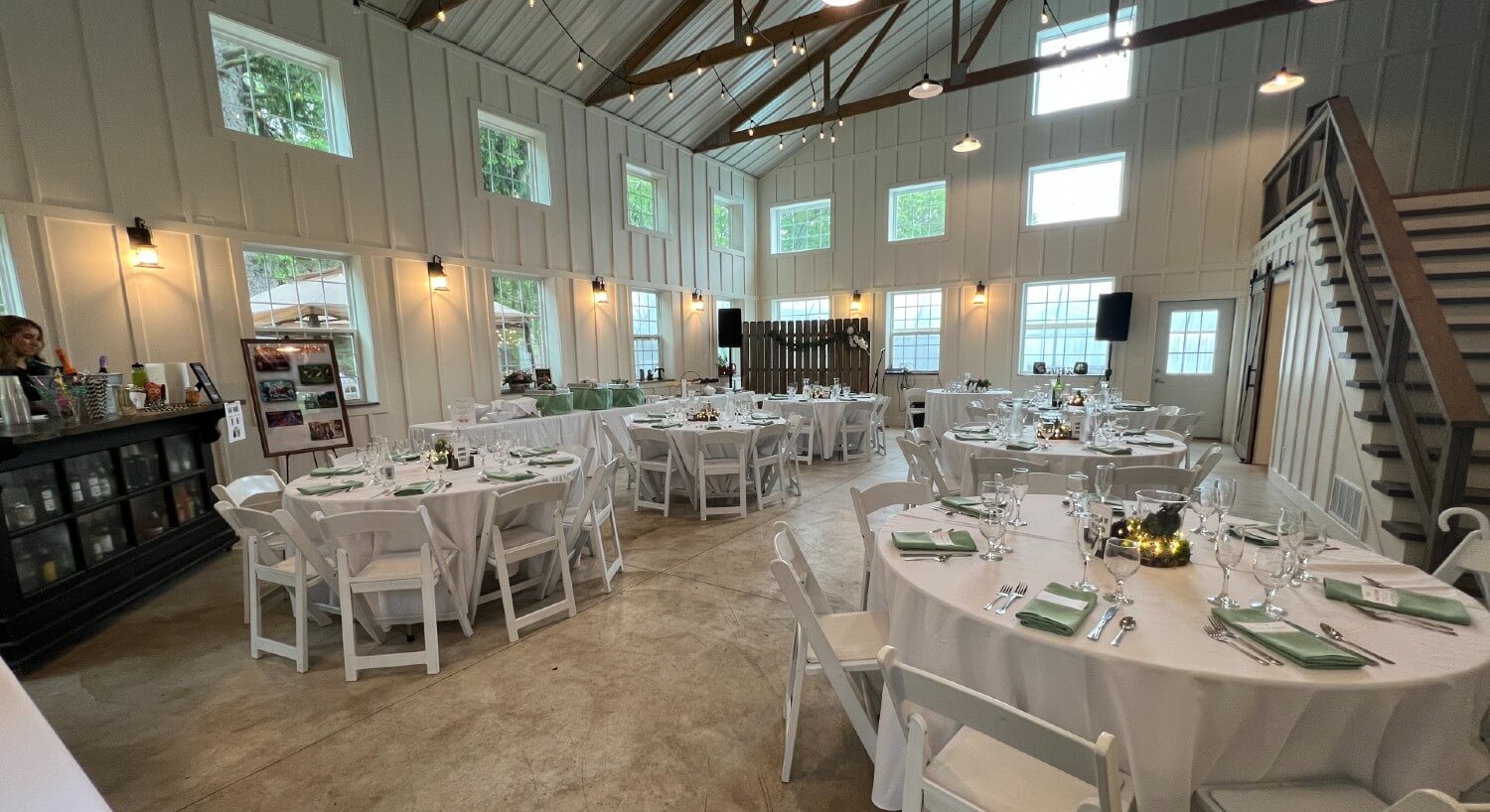 A large white barn venue with wood beams set up for a wedding event with several round tables