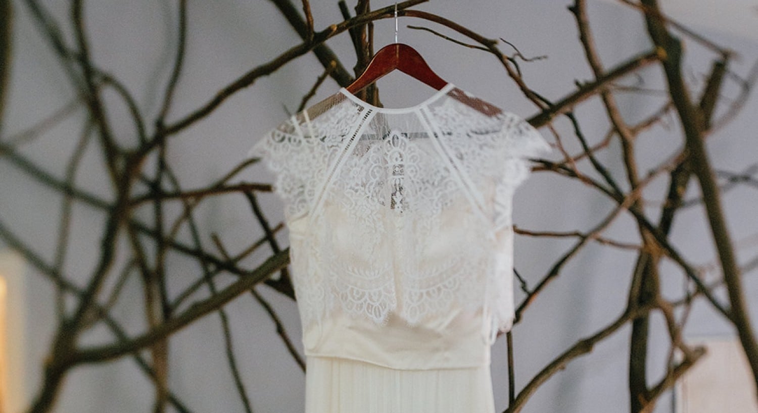 A gorgeous lace dress hanging on a wooden hanger with branches behind