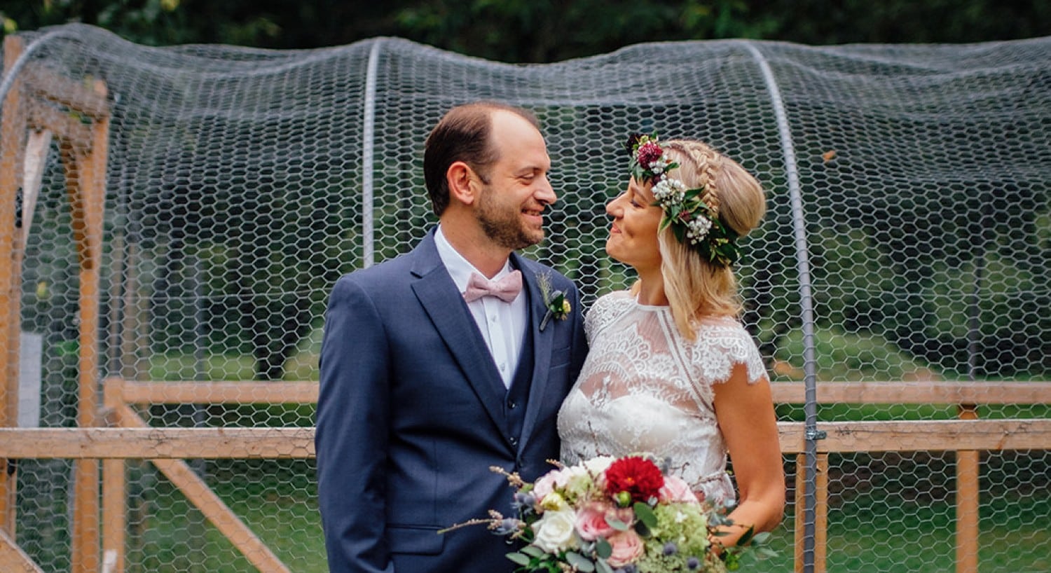 A bride with a gorgeous bouquet and floral headpiece with her groom standing outdoors
