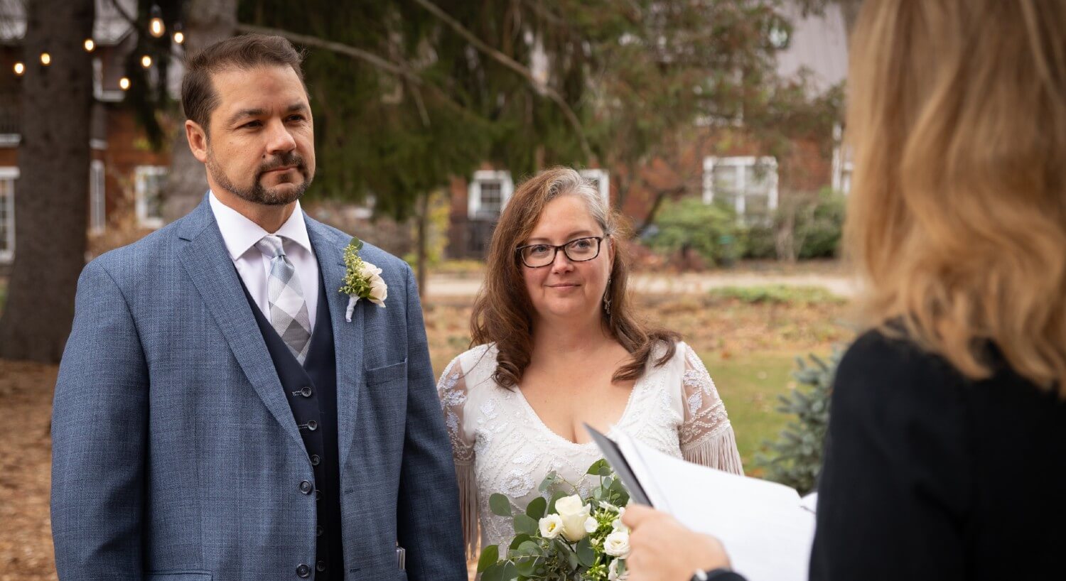 A bride and groom standing outside in front of a female officiant